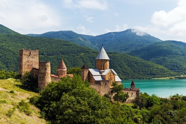 Historic stone monastery beside a lake and green mountains, ideal for a Georgia holiday package from Dubai.