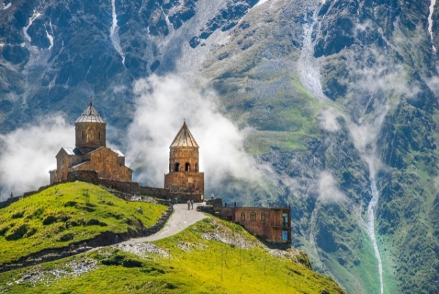 Scenic mountain church in Georgia surrounded by clouds and green hills, ideal for a Georgia holiday package from Dubai.