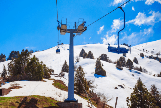 Passengers riding an open-air chairlift up the snow-covered slopes of the Chimgan Mountains.