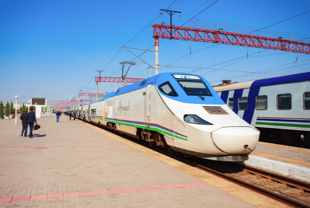 Afrosiyob high-speed train at a sunny station platform in Uzbekistan with passengers walking by.