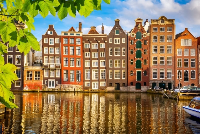Colorful historic Dutch canal houses in Amsterdam reflecting in the water under a clear blue sky.