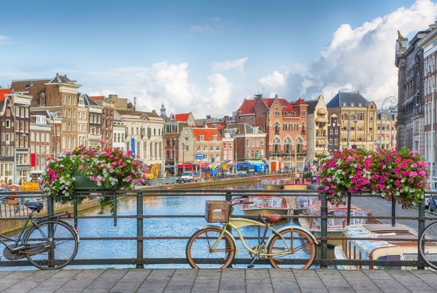 Amsterdam canal view with bicycles on a bridge and historic Dutch architecture under a blue sky.