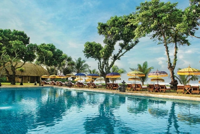 Large turquoise swimming pool at a Bali luxury resort with traditional thatched-roof pavilions and colorful sun umbrellas for UAE travelers.