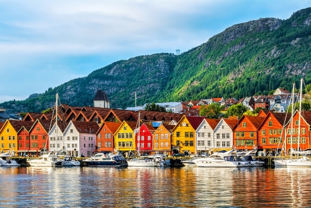 Colorful historic wooden buildings of Bryggen at Bergen harbor, Norway, under a blue sky with green mountain backdrop.
