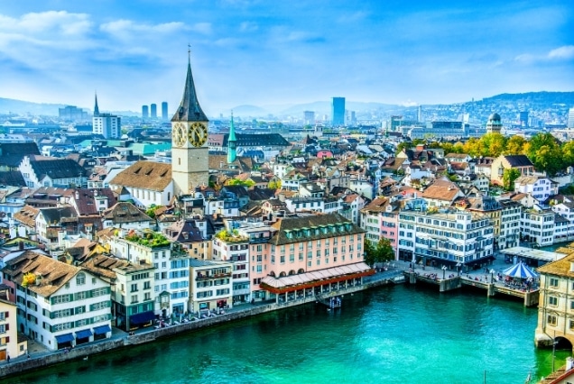 Panoramic view of Zurich, Switzerland, featuring the St. Peter's Church clock tower and colorful buildings along the Limmat river.