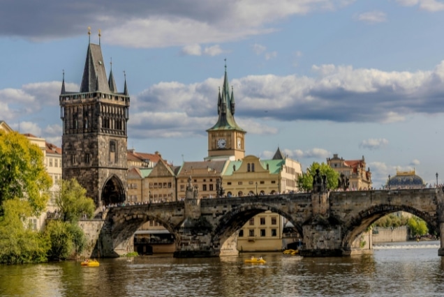 Scenic view of the Charles Bridge and Old Town Bridge Tower over the Vltava River in Prague under a cloudy sky.