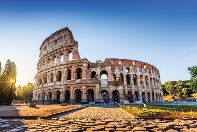 Sunlight glowing through the ancient arches of the Roman Colosseum in Italy under a clear blue sky, featured in a multi-country European tour package.