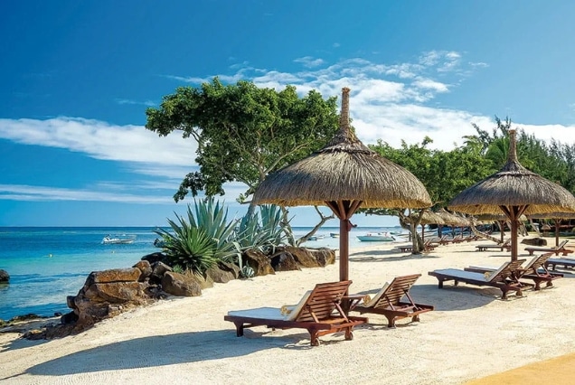 Luxury beach resort in Mauritius with straw umbrellas and wooden lounge chairs on white sand under a clear blue sky.