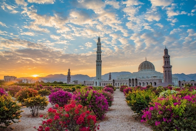 Sunset view of Sultan Qaboos Grand Mosque in Muscat with flower gardens, ideal for Oman e-visa travelers from Dubai.