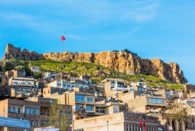 View of Mardin Old City houses in Turkey with the historic Mardin Castle on the hilltop under a clear blue sky.