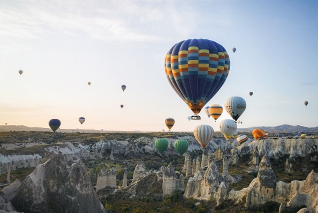 Multicolored hot air balloons flying over the fairy chimneys and rock formations of Cappadocia, Turkey at sunrise.