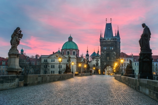 Sunrise at Charles Bridge in Prague featuring the Old Town Bridge Tower and historical religious statues.