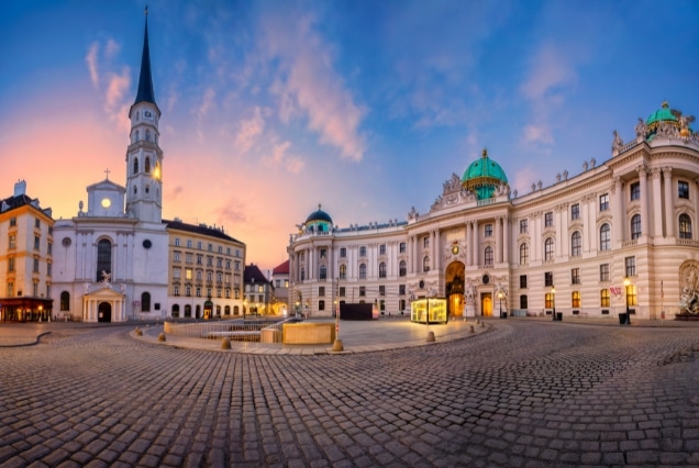 Panoramic view of Michaelerplatz in Vienna at sunset, featuring Hofburg Palace entrance and St. Michael's Church.