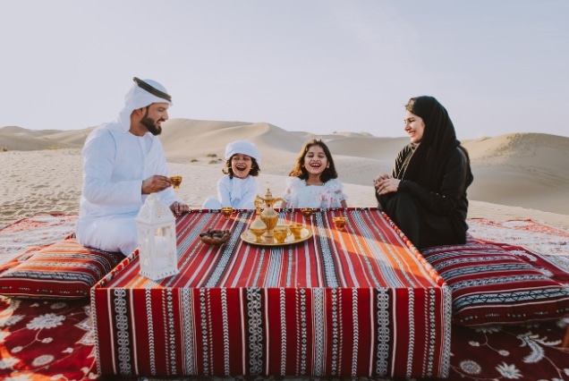 An Arab family sharing traditional coffee and dates on a red carpet amid the golden Dubai desert dunes.