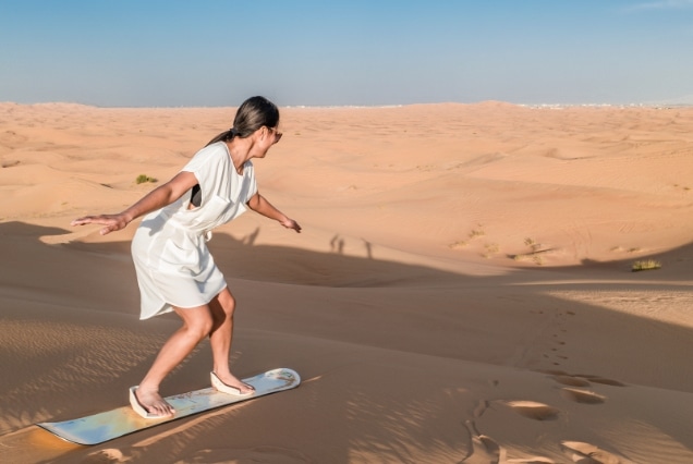 A woman sandboarding down a steep sand dune during a desert safari adventure in the UAE.