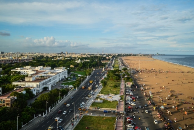 High-angle aerial view of Marina Beach in Chennai featuring the long sandy coastline, city road, and urban skyline.