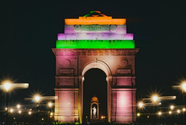 Grand view of the India Gate war memorial in New Delhi under a bright blue sky with green lawns in the foreground.