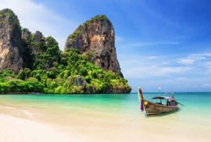 Thai longtail boat in turquoise waters near Krabi limestone cliffs, showcasing Thailand holiday packages from Dubai.