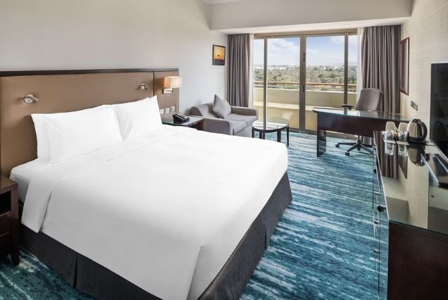 Guest room with large bed, desk and balcony view at Radisson Blu Hotel & Resort, Al Ain