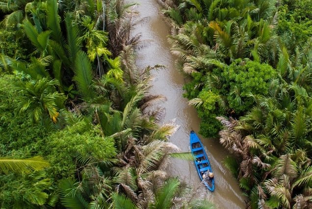 Aerial view of a boat on a Mekong Delta canal surrounded by palms – Vietnam Holiday Package